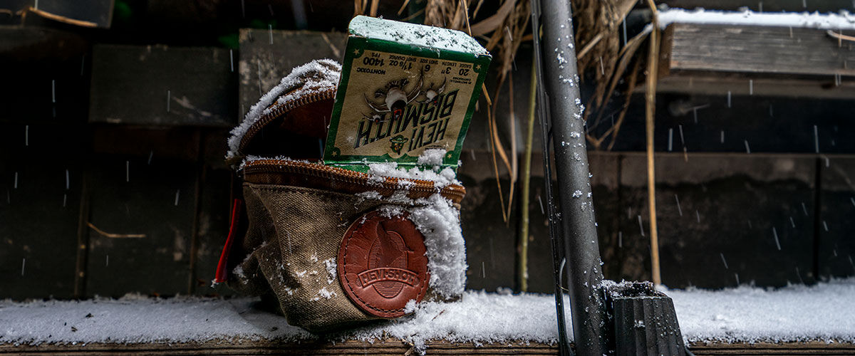 HEVI-Bismuth in a Shell Bag next to a shotgun in the snow