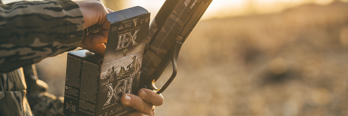 hunter opening box of HEVI-XII while holding a shotgun
