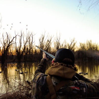 Seth aiming his shotgun at some ducks from within a duck blind