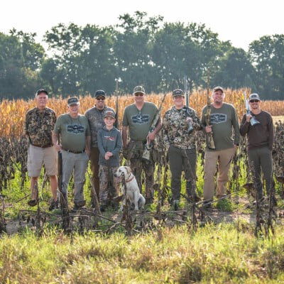 Family of hunters standing in a row in front of a dried corn field