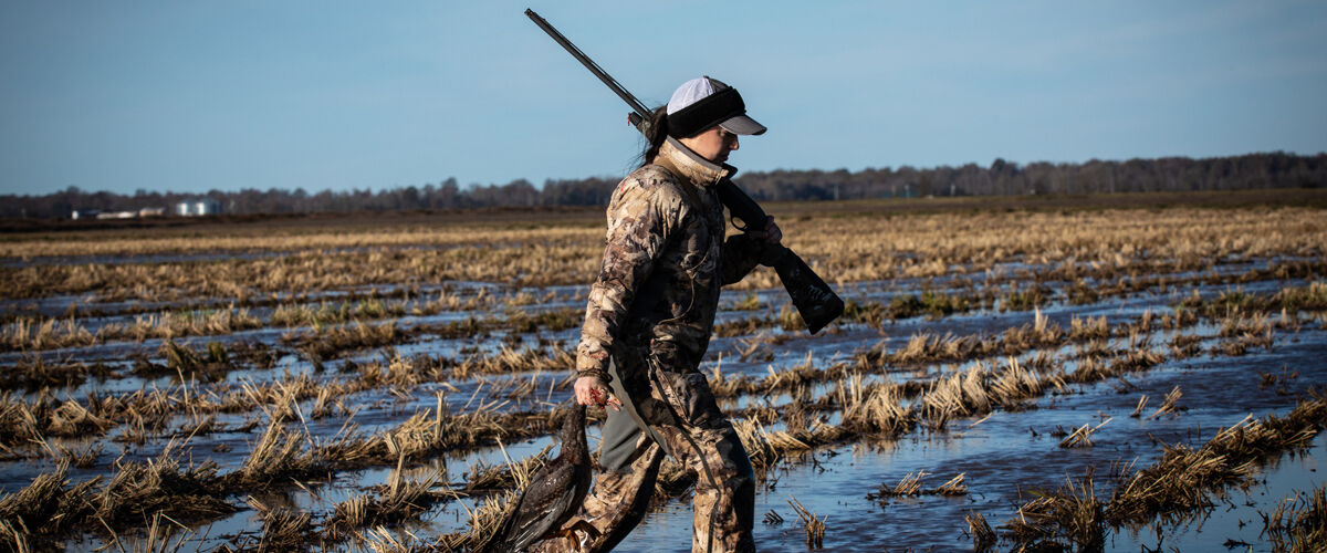 Jennifer Richard walking through a field with a shotgun on her shoulder