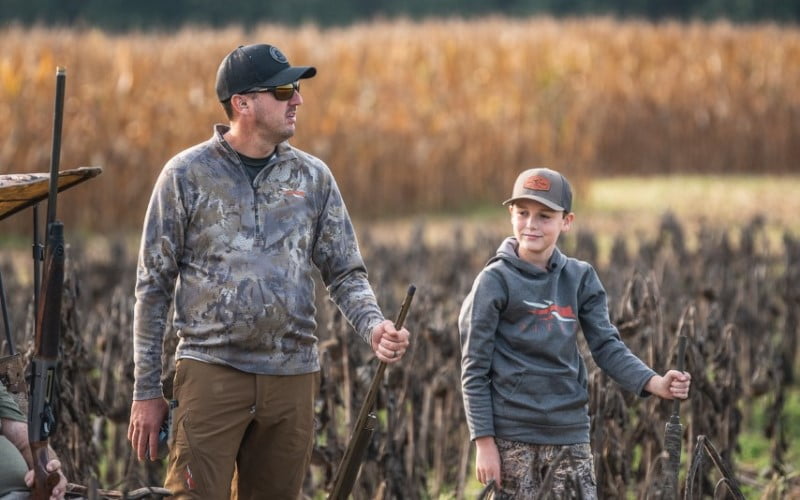 father and son standing in front of a field of dried corn