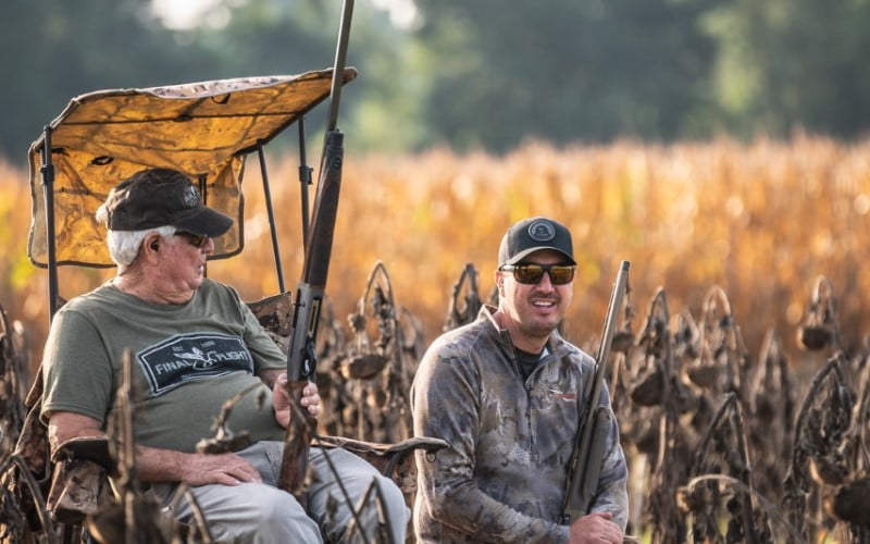 father and son sitting and knelling in front of a field of dried corn